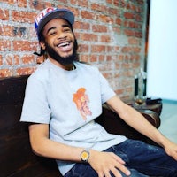 a young man wearing a hat and t - shirt sitting on a bench